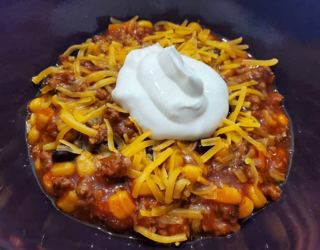 Taco soup topped with shredded cheese and sour cream