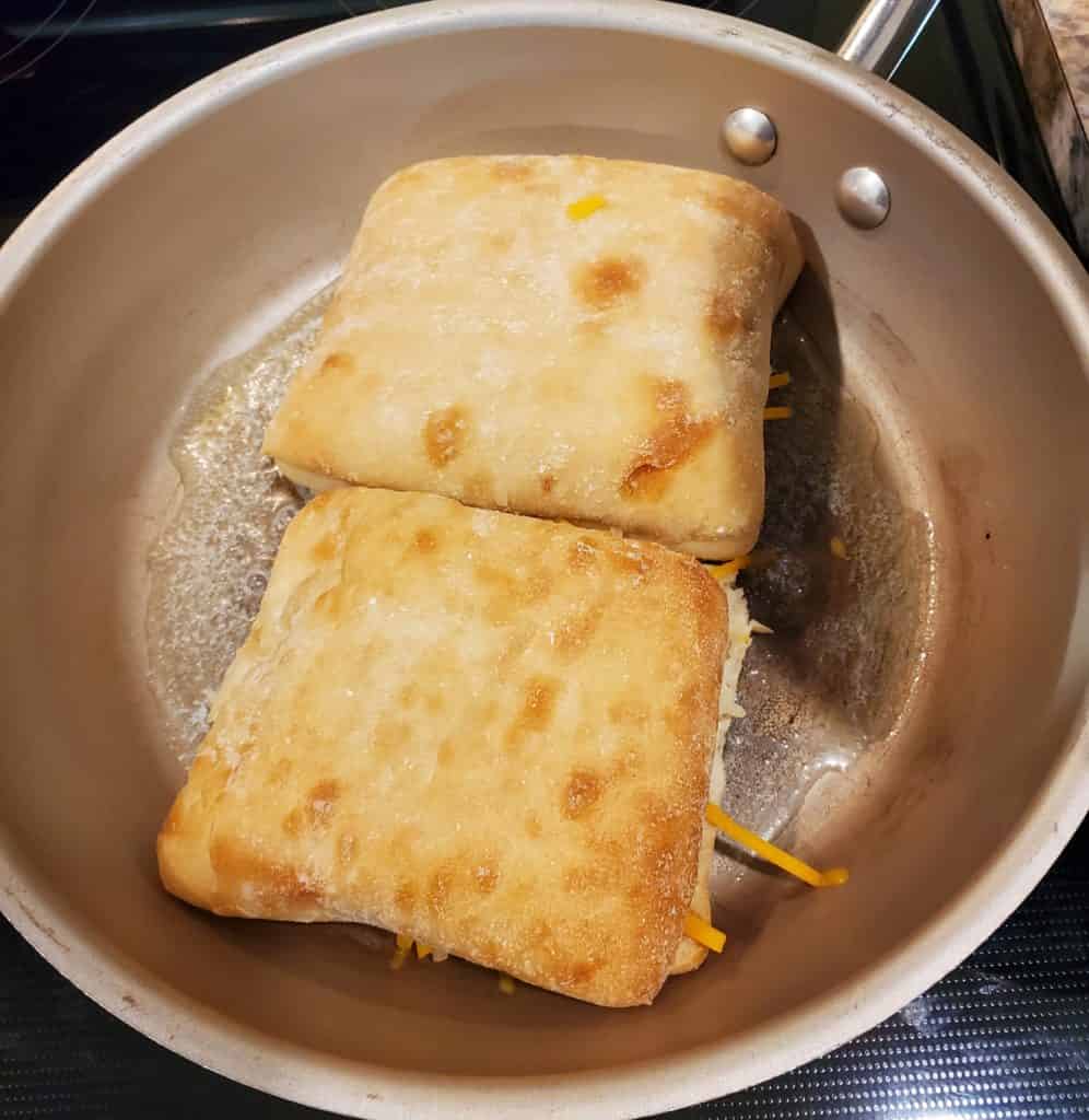 Two ciabatta grilled cheese sandwiches in a skillet with melted butter and oil