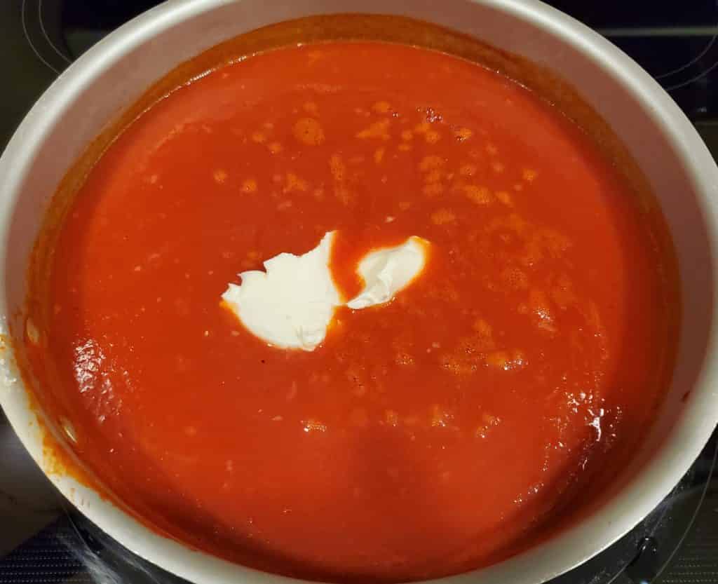 Cream cheese being added to the creamy tomato soup