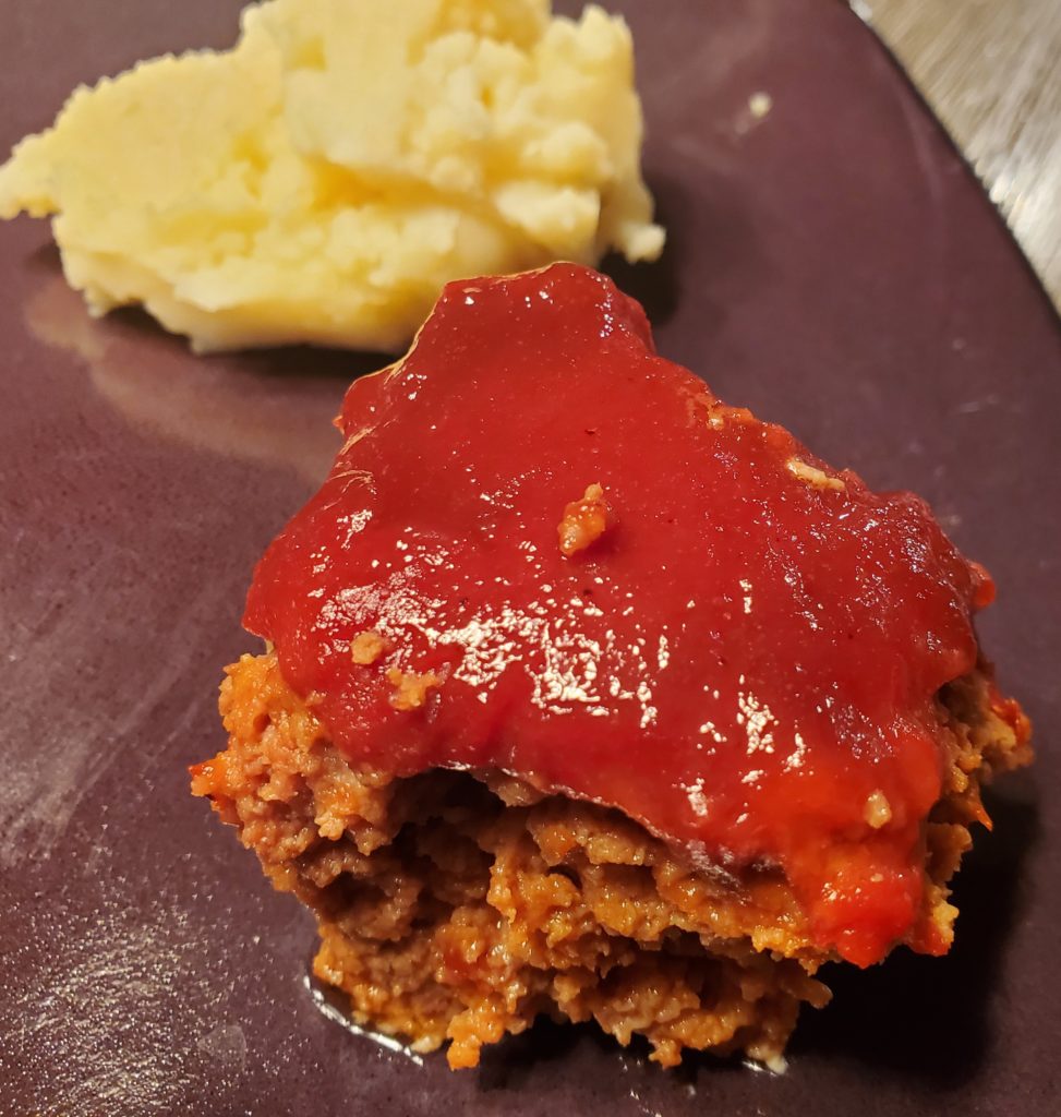 A slice of delicious meatloaf with ketchup glaze alongside some mashed potatoes