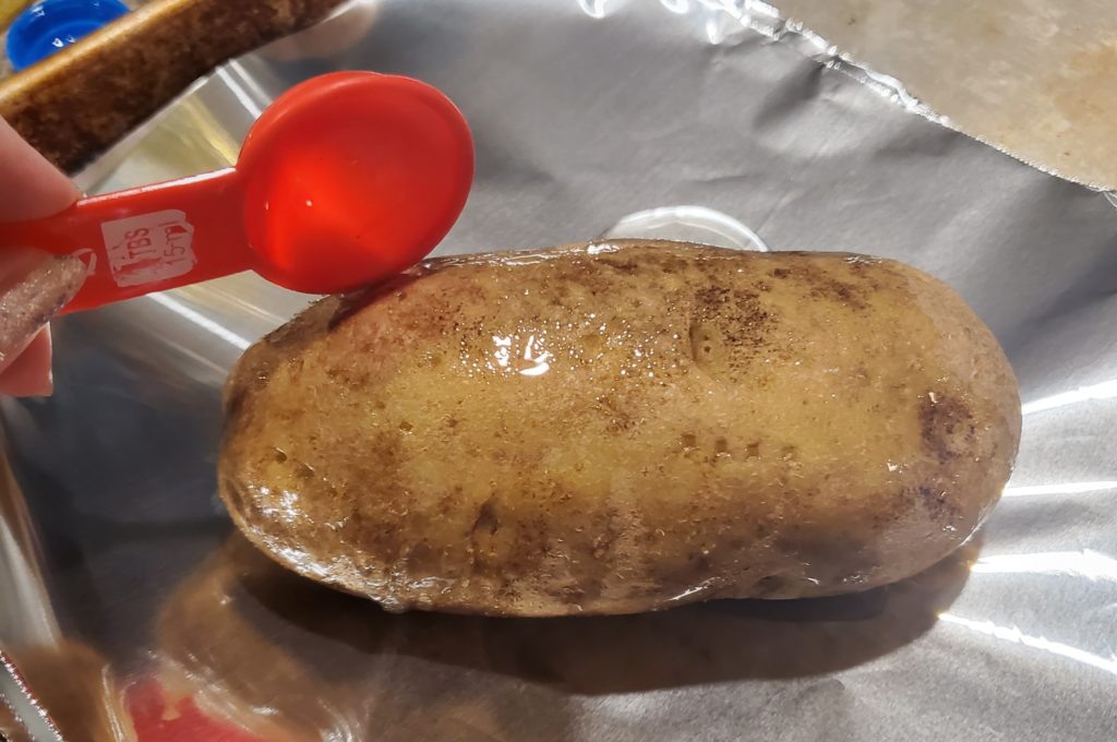 A baked potato being drizzled with vegetable oil
