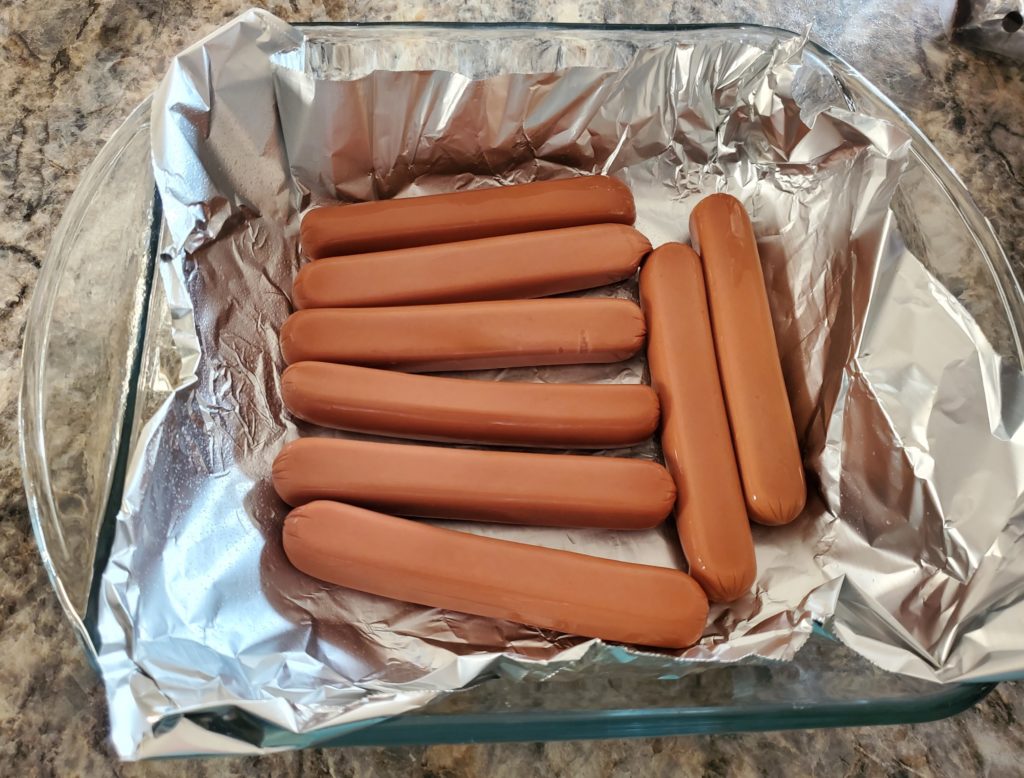 Uncooked hot dogs in a foil-lined pan ready to go into the oven