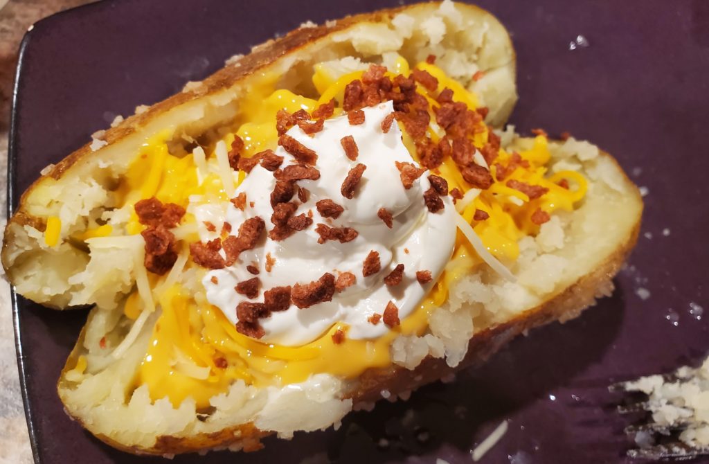 A finished baked potato loaded with butter, cheese, sour cream and bacon bits