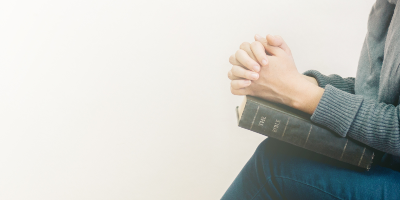 Woman with her hands folded in prayer on top of a Bible