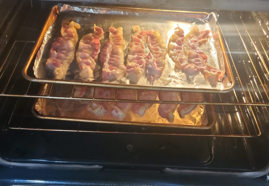 The bacon in the oven, halfway cooked and ready to switch racks