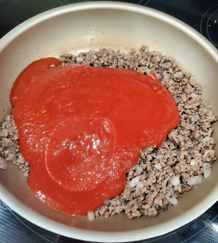 Adding the tomato sauce for the sloppy joe sauce to the skillet with the ground beef and onions
