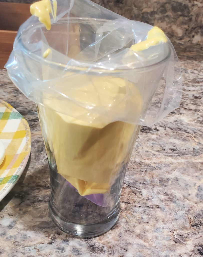 The deviled egg filling in a piping bag in a tall drinking glass