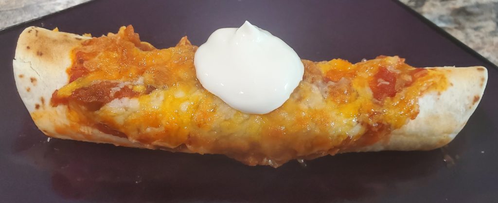 A beef enchilada on a plate topped with sour cream