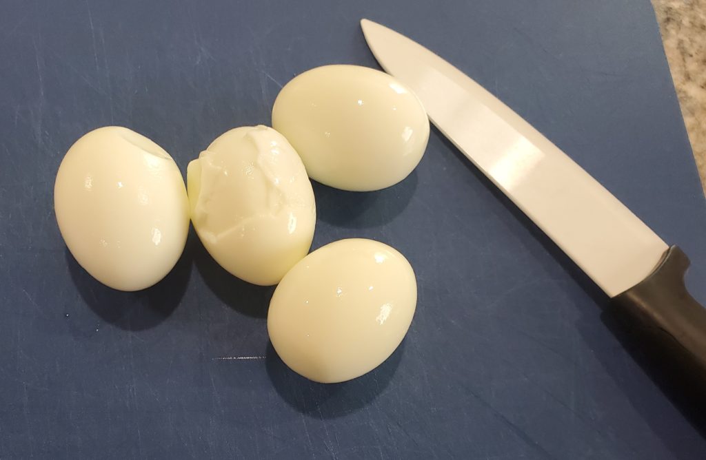 Four boiled eggs on a cutting board with a knife